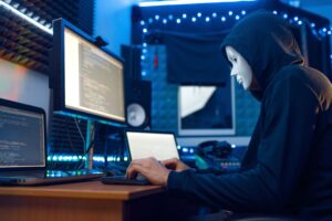 Hacker in mask and hood typing at a computer